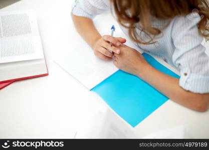 education, people, children and learning concept - girl with book writing to notebook at school. girl with book writing to notebook at school