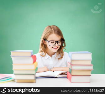 education, people, children and school concept - happy student girl in eyeglasses reading book over green chalk board background