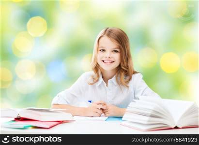 education, people, children and school concept - happy student girl sitting at table with books and writing in notebook over green lights background