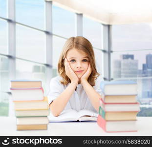 education, people, children and school concept - little student girl sitting at table with books and writing in notebook over classroom background