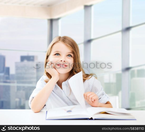 education, people, children and school concept - little student girl sitting at table with books and writing in notebook over classroom background