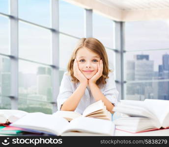 education, people, children and school concept - little student girl sitting at table with books and writing in notebook over classroom background