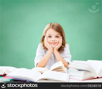 education, people, children and school concept - little student girl sitting at table with books over green chalk board background