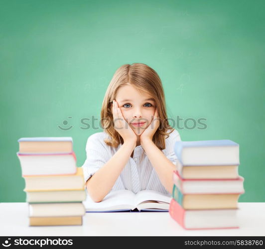 education, people, children and school concept - little student girl sitting at table with books over green chalk board background