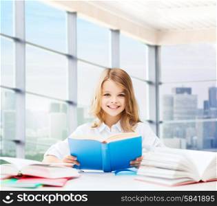 education, people, children and school concept - little student girl sitting at table with books and writing in notebook over classroom background