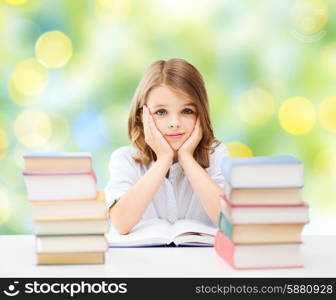 education, people, children and school concept - little student girl sitting at table with books over green lights background