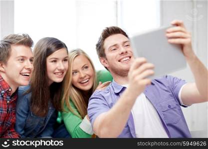 education, people, friendship, technology and learning concept - group of happy high school students or classmates with tablet pc computer taking selfie in classroom