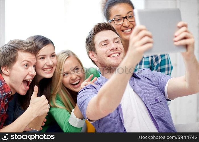 education, people, friendship, technology and learning concept - group of happy international high school students with tablet pc computer taking selfie in classroom and showing thumbs up