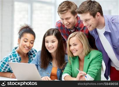 education, people, friendship, technology and learning concept - group of happy international high school students or classmates with laptop computer in classroom