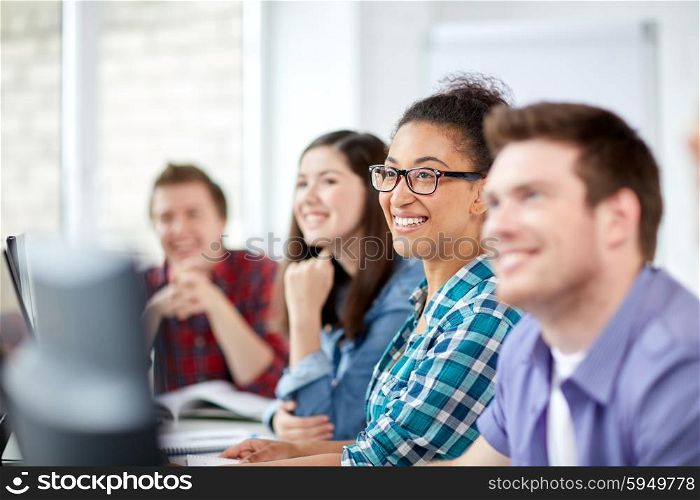 education, people, friendship, technology and learning concept - group of happy international high school students or classmates in computer class