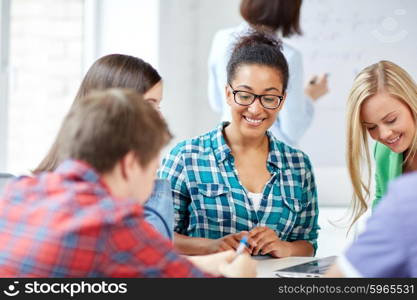 education, people, friendship, technology and learning concept - group of happy international high school students or classmates with workbook learning in classroom