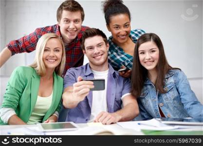 education, people, friendship, technology and learning concept - group of happy international high school students or classmates with smartphone taking selfie in classroom