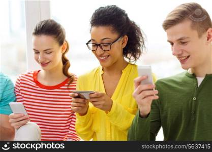 education, relationships and technology concept - three smiling students with smartphone at school