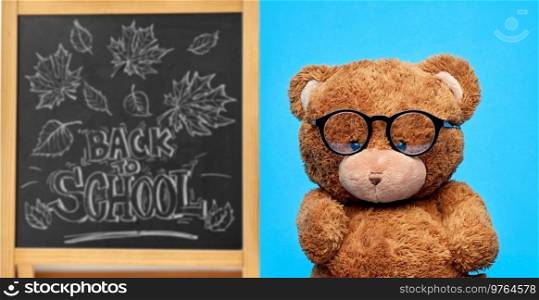 education, school and childhood concept - brown teddy bear in glasses over chalkboard on background. teddy bear in glasses over school chalkboard