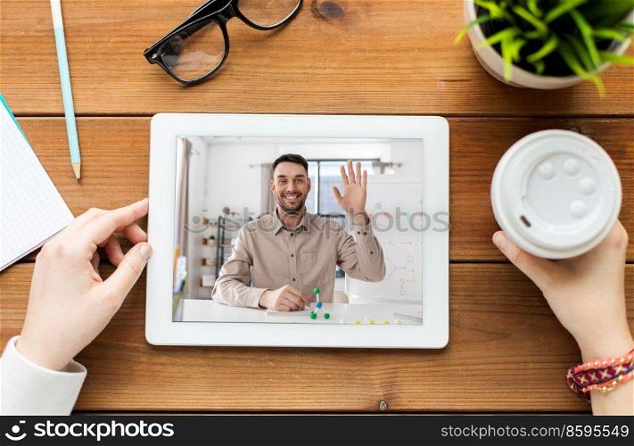 education, school and distance learning concept - close up of hands with chemistry teacher on tablet pc computer screen and coffee cup on wooden table. close up of hands with teacher on tablet pc screen