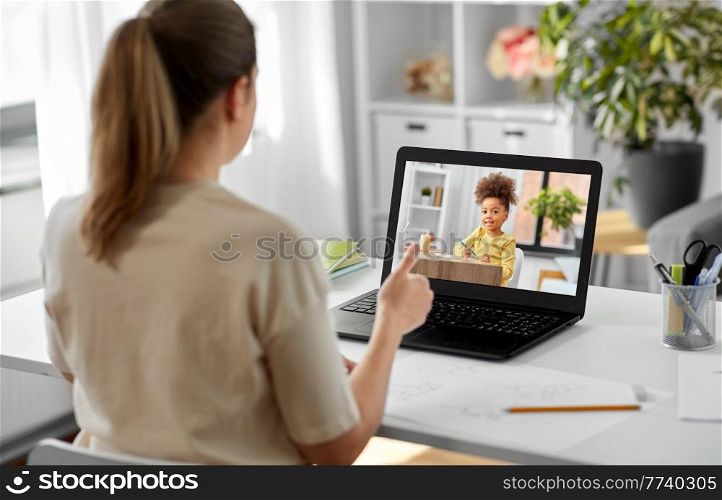 education, school and distant learning concept - female teacher with laptop computer having online class with little student girl at home and showing thumbs up. female teacher with laptop having online class