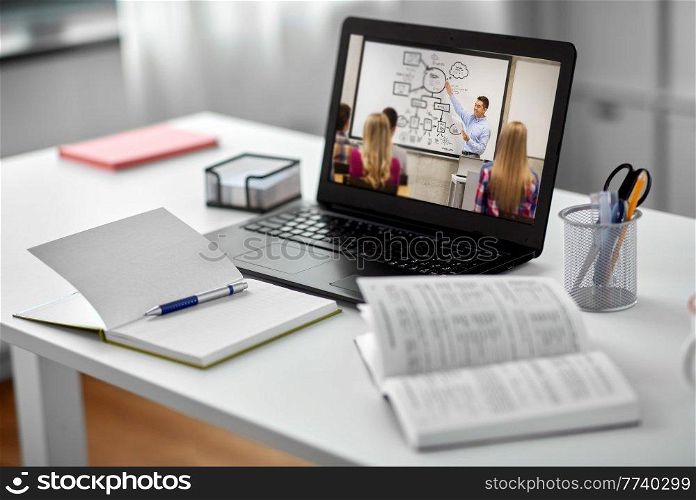 education, school and distant learning concept - open laptop computer with teacher and students on screen, notebook and book on table at home. laptop&rsquo;s screen with teacher and students on table