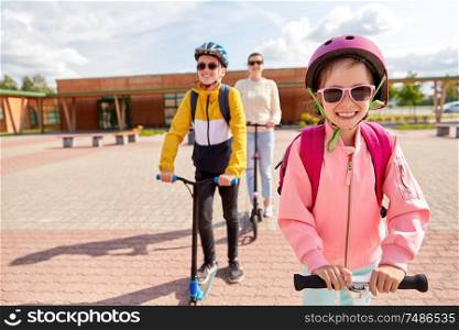education, school and family concept - happy daughter, son and mother riding scooters outdoors. happy school children with mother riding scooters