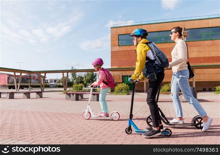 education, school and family concept - happy daughter, son and mother riding scooters outdoors. happy school children with mother riding scooters