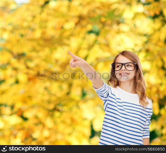 education, school and imaginary screen concept - cute little girl in eyeglasses pointing in the air or imaginary screen