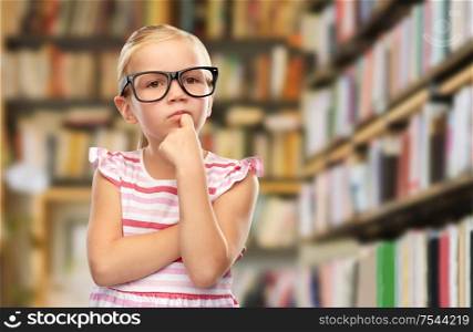 education, school and learning concept - cute little girl in black glasses over library book shelves background. little girl in black glasses thinking at library