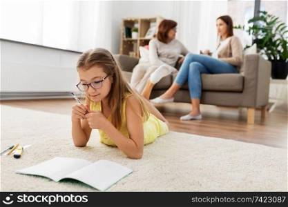 education, school and learning concept - student girl lying on floor and writing to notebook at home. student girl writing to notebook at home