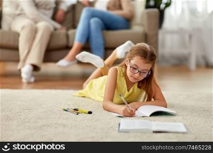 education, school and learning concept - student girl lying on floor and writing to notebook at home. student girl writing to notebook at home