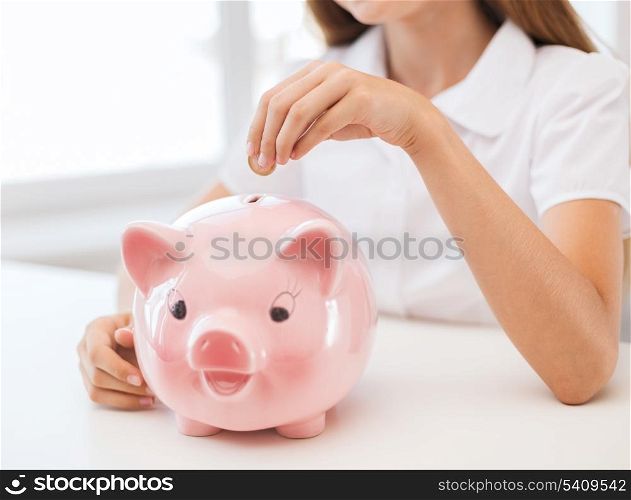 education, school and money saving concept - smiling child putting coin into big piggy bank