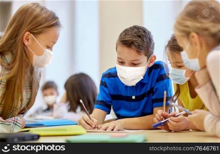 education, school and pandemic concept - group of students wearing face protective medical mask for protection from virus disease with pencils and papers writing at classroom. group of students in masks learning at school