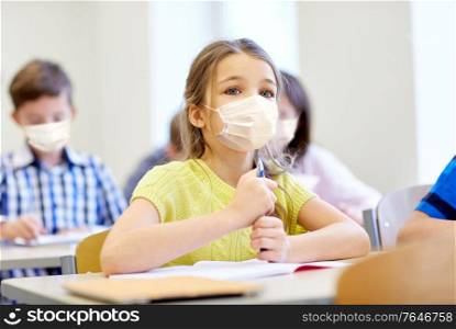 education, school and pandemic concept - student girl wearing face protective medical mask for protection from virus disease with group of classmates on lesson at classroom. little student girl in mask on lesson at school