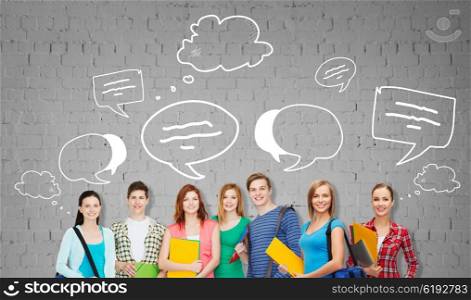 education, school and people concept - group of smiling teenage students with folders and school bags over gray brick wall background with text bubbles