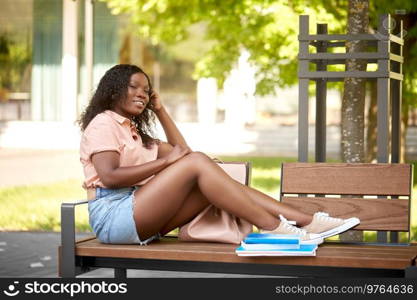 education, school and people concept - happy smiling african american student girl with backpack and books sitting on bench in city. african student girl with bag and books in city