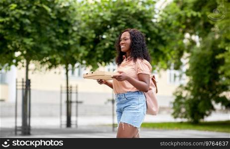 education, school and people concept - happy smiling african american student girl walking with takeaway pizza box on city street. african student girl with takeaway pizza in city