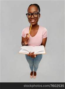 education, school and people concept - happy smiling african american woman in glasses with notebook and pencil over grey background. happy african american woman with notebook