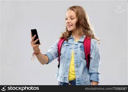 education, school and people concept - happy smiling teenage student girl with bag taking selfie by smartphone over grey background. teenage student girl taking selfie by smartphone