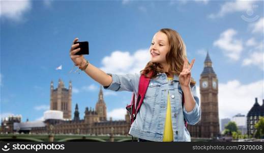 education, school and people concept - happy smiling teenage student girl with bag taking selfie by smartphone and showing peace over big ben in city of london background. teenage student girl taking selfie by smartphone
