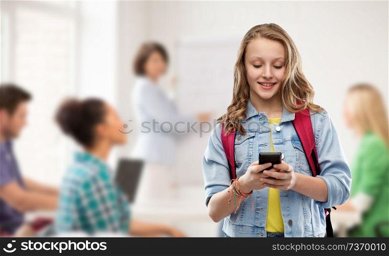 education, school and people concept - happy smiling teenage student girl with bag and smartphone over classroom background. teen student girl with school bag and smartphone