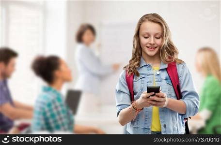 education, school and people concept - happy smiling teenage student girl with bag and smartphone over classroom background. teen student girl with school bag and smartphone