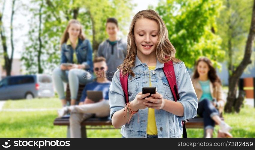 education, school and people concept - happy smiling teenage student girl with bag and smartphone over group of friends background. teen student girl with school bag and smartphone