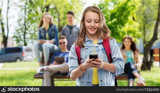 education, school and people concept - happy smiling teenage student girl with bag and smartphone over group of friends background. teen student girl with school bag and smartphone
