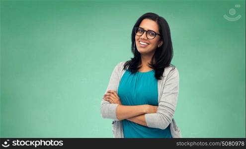 education, school and people concept - happy smiling young indian student woman or teacher in glasses over green chalkboard background. happy smiling young indian woman in glasses