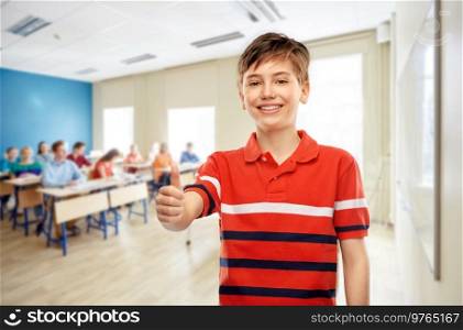 education, school and people concept - portrait of happy smiling student boy in red polo t-shirt showing thumbs up over classroom background. happy student boy showing thumbs up at school