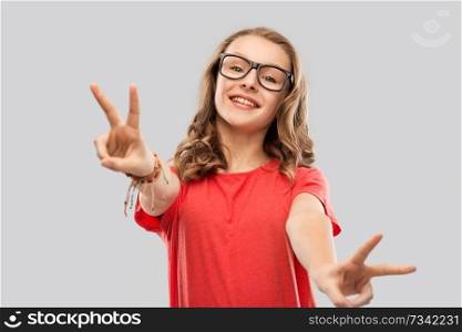 education, school and people concept - smiling teenage student girl in glasses and red t-shirt showing peace hand sign over grey background. smiling student girl in glasses showing peace