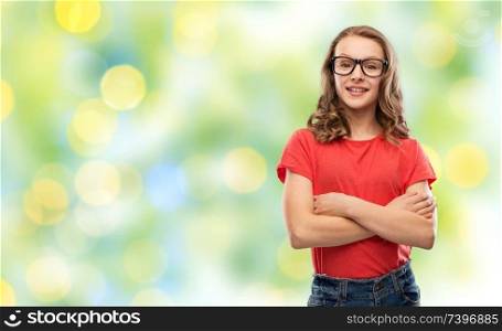 education, school and people concept - smiling teenage student girl in glasses and red t-shirt with crossed arms over summer green lights background. smiling student girl in glasses over green lights