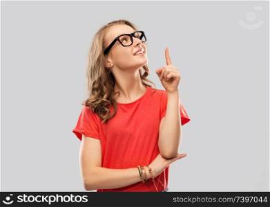 education, school and people concept - smiling teenage student girl in glasses and red t-shirt pointing finger up over grey background. smiling student girl in glasses pointing finger up