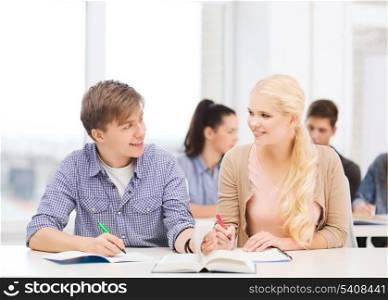 education, school and people concept - two teenagers with notebooks and book looking at each other at school