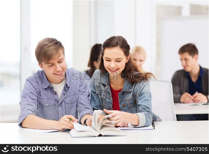 education, school and people concept - two teenagers with notebooks and book at school