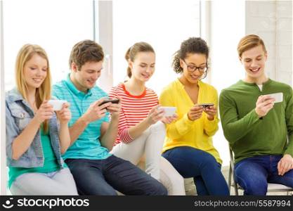 education, school and technology concept - smiling students with smartphone texting at school