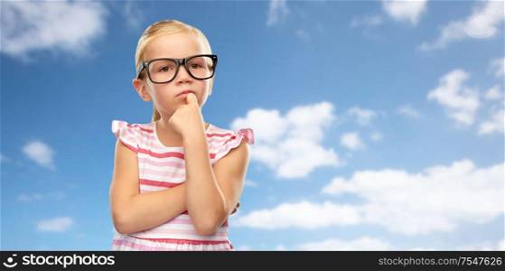 education, school and vision concept - cute little girl in black glasses over blue sky and clouds background. cute little girl in black glasses thinking