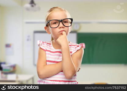 education, school and vision concept - cute little girl in black glasses over classroom background. cute little girl in black glasses thinking